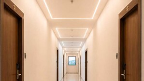 Un largo y estrecho pasillo de hotel con puertas de madera a ambos lados, suelo de mármol e iluminación empotrada en el techo.