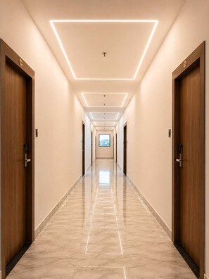 Ein langer, schmaler Hotelkorridor mit Holztüren an beiden Seiten, einem Marmorboden und Einbauleuchten an der Decke.