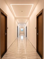 Un largo y estrecho pasillo de hotel con puertas de madera a ambos lados, suelo de mármol e iluminación empotrada en el techo.