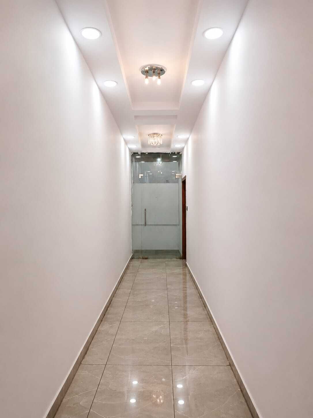 A narrow hallway with a tiled floor, white walls, and recessed lighting.