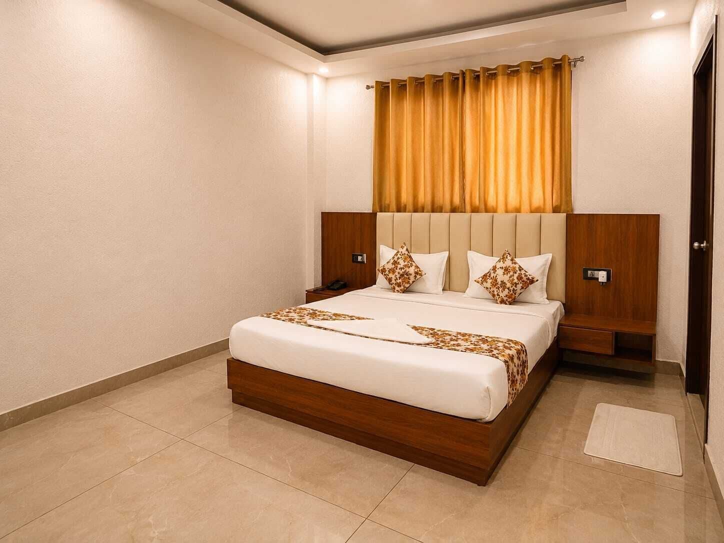 Habitación de hotel con una cama grande, cabecera de madera, dos mesitas de noche y una cortina.