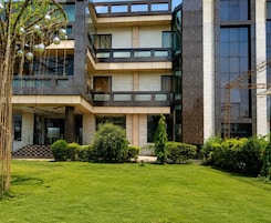 Un edificio moderno de varios pisos con un patio central, ventanas amplias y un césped cuidado.