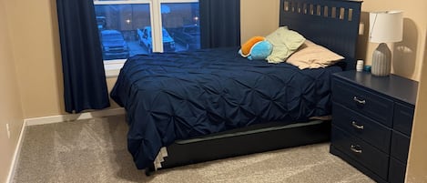 A bedroom with a bed, a nightstand, a lamp, a window with curtains, and a ceiling fan.