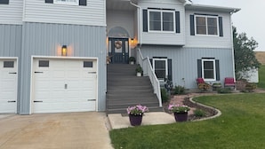 Ein zweistöckiges Haus mit einer Veranda, einer Garage und einem angelegten Garten.