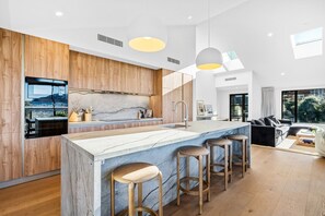 A modern kitchen with a marble island, wooden cabinets, and a large window overlooking a cityscape. - Aspen Ridge by MajorDomo | Fernhill Villa with Lake Views, Infrared Sauna, Spa Pool & Outdoor Fireplace (Queenstown)
