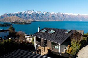 A modern house with a sloped roof, large windows, and a view of a lake and mountains. - Aspen Ridge by MajorDomo | Fernhill Villa with Lake Views, Infrared Sauna, Spa Pool & Outdoor Fireplace (Queenstown)