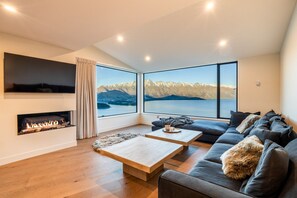 A modern living room with a fireplace, a sofa, a coffee table, and large windows offering a mountain view. - Aspen Ridge by MajorDomo | Fernhill Villa with Lake Views, Infrared Sauna, Spa Pool & Outdoor Fireplace (Queenstown)