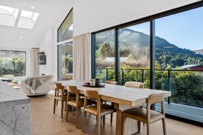 Ein stilvolles Esszimmer mit großem Tisch und Stühlen, großen Fenstern mit Bergblick und einer gemütlichen Sitzecke mit Sofa und Couchtisch.