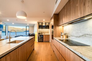 A modern kitchen with wooden cabinets, a marble countertop, and a view of the sea. - Aspen Ridge by MajorDomo | Fernhill Villa with Lake Views, Infrared Sauna, Spa Pool & Outdoor Fireplace (Queenstown)