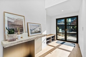 A modern interior with a built-in bench, framed pictures, a potted plant, and a view through a glass door. - Aspen Ridge by MajorDomo | Fernhill Villa with Lake Views, Infrared Sauna, Spa Pool & Outdoor Fireplace (Queenstown)