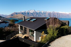A modern house with a sloped roof, large windows, and a view of mountains and a lake. - Aspen Ridge by MajorDomo | Fernhill Villa with Lake Views, Infrared Sauna, Spa Pool & Outdoor Fireplace (Queenstown)