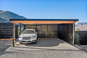 A covered parking area with a vehicle, a metal fence, and a mountainous backdrop. - Aspen Ridge by MajorDomo | Fernhill Villa with Lake Views, Infrared Sauna, Spa Pool & Outdoor Fireplace (Queenstown)