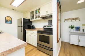 A compact kitchen with white cabinetry, a stainless steel refrigerator, a black oven, and a countertop with a coffee maker. - Waterfront Tahoe Keys Condo. Private Boat Dock, Lake Views & Family Friendly (South Lake Tahoe)