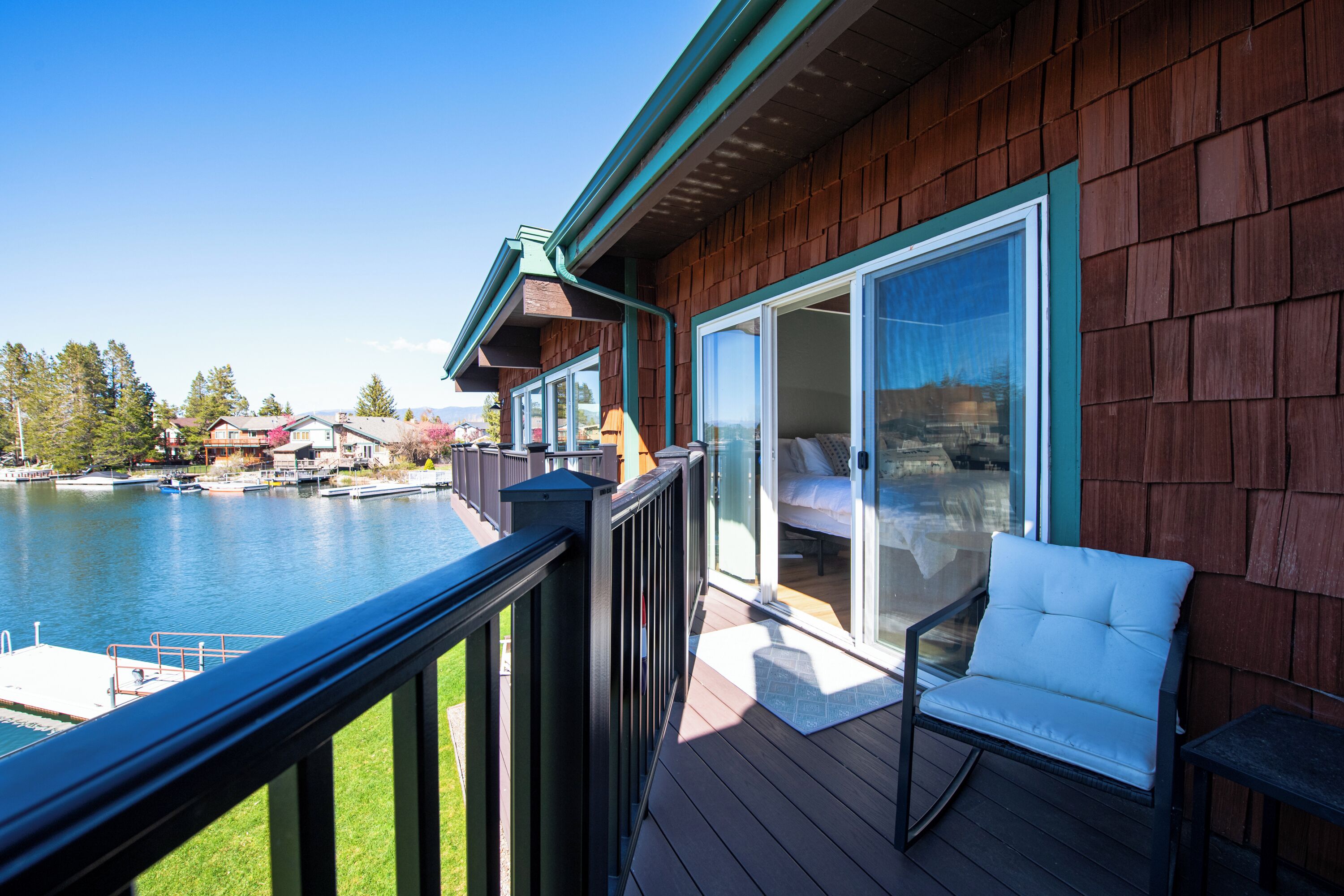 Une terrasse en bois avec une porte vitrée donnant sur une chambre, d’où l’on a vue sur une étendue d’eau et des bateaux.
