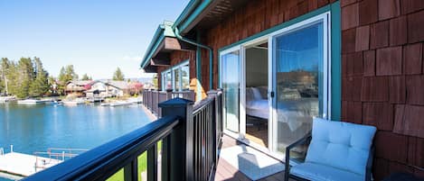 Une terrasse en bois avec une porte vitrée donnant sur une chambre, d’où l’on a vue sur une étendue d’eau et des bateaux.