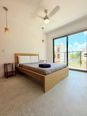 Un dormitorio con cama, ventilador de techo y vistas a edificios a través de amplios ventanales.