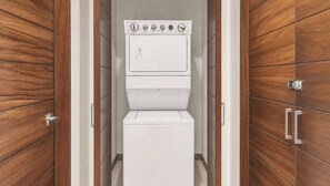 A laundry room with a stacked washer and dryer, wooden paneling, and a door with a handle. - Beachfront Luxury 3 BR Condo in Diamante Dunes (Cabo San Lucas)
