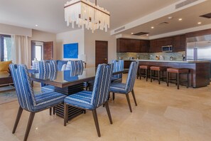 A modern kitchen with dark wood cabinets, a stainless steel refrigerator, and a bar area with stools. - Beachfront Luxury 3 BR Condo in Diamante Dunes (Cabo San Lucas)