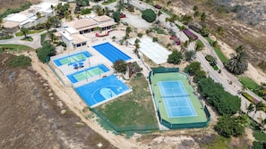 Eine Vogelperspektive zeigt eine Wohngegend mit mehreren Tennisplätzen, einem Schwimmbad und umliegender Grünfläche.