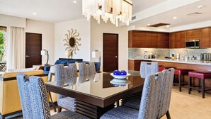 A modern dining area with a glass-top table, patterned chairs, and a decorative wall piece. - Beachfront Luxury 3 BR Condo in Diamante Dunes (Cabo San Lucas)