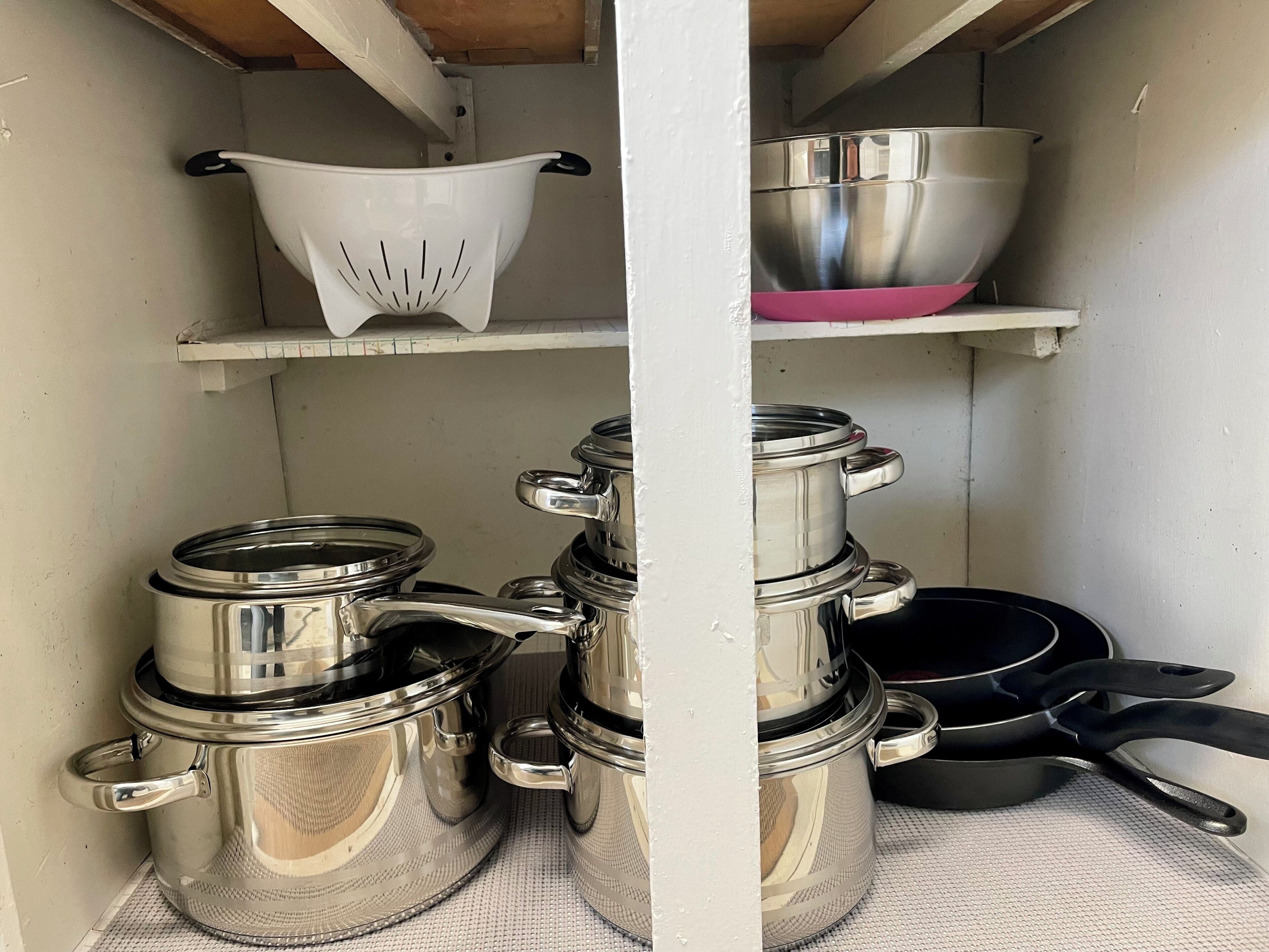 A kitchen shelf with stainless steel cookware, including pots and a colander.