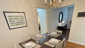 A dining area with a table set for four, a chandelier, and a framed picture on the wall.