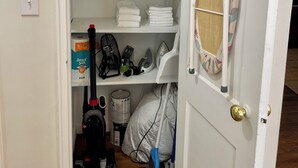 A storage closet with shelves containing folded towels, pillows, and cleaning supplies.