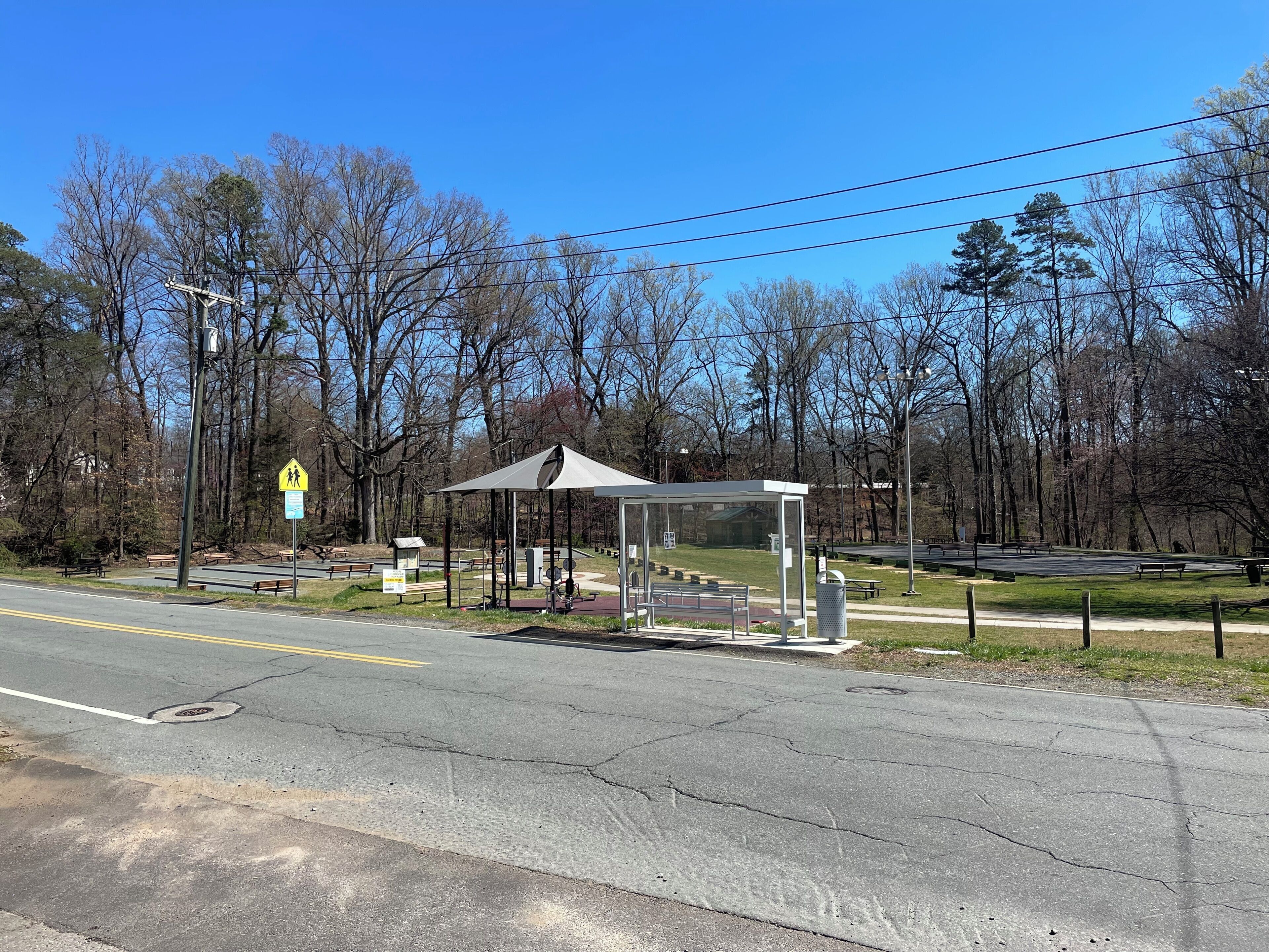 A pedestrian crossing sign, a covered shelter, and a park with benches and trees.