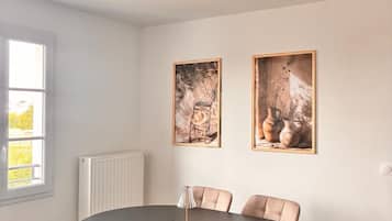 Un comedor con una mesa redonda, seis sillas y dos obras de arte enmarcadas en la pared.