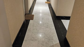 Un pasillo de hotel con suelo de mármol, una puerta al final y una alfombra de entrada en el suelo.