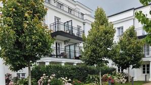 Un bâtiment à la façade blanche, un chemin de gravier et un jardin agrémenté de fleurs roses.