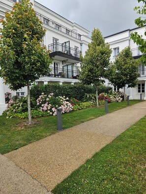 A building with a white facade, a gravel pathway, and a garden with pink flowers. - 3-room apartment next to Disney and Vallée Village with a 7.4 kWh charging station (Serris)