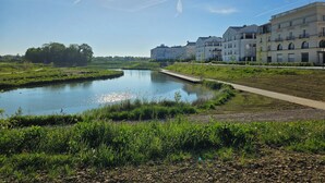 Une vue sur le fleuve, avec un ciel dégagé, une étendue d’eau calme et une rangée d’immeubles résidentiels à plusieurs étages.