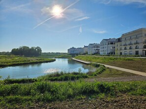 A riverside view with a clear sky, a calm water body, and a row of multi-story residential buildings. - 3-room apartment next to Disney and Vallée Village with a 7.4 kWh charging station (Serris)