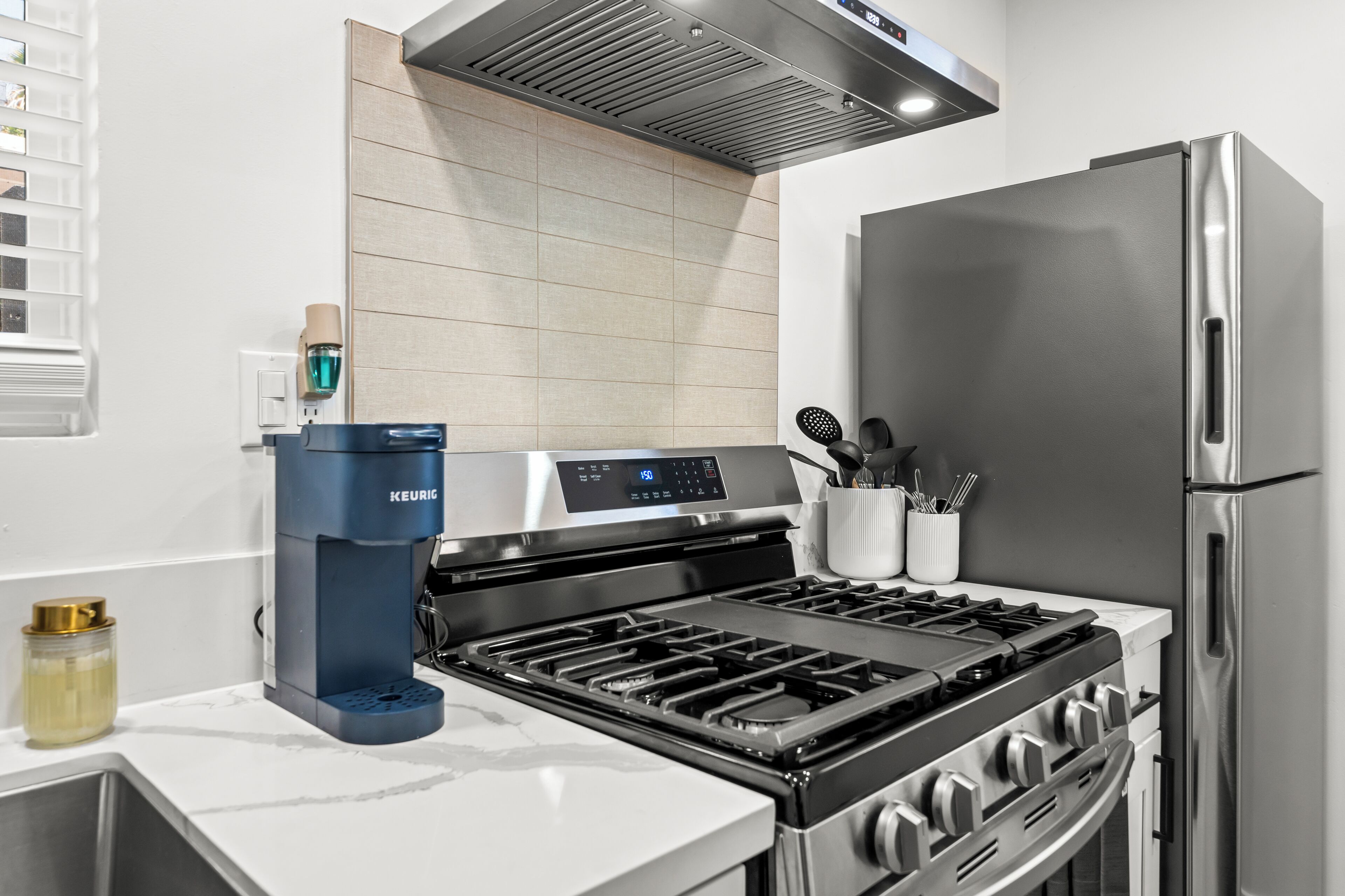 A modern kitchen with a stainless steel stove, a built-in oven, a coffee maker, and a refrigerator.