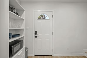 A white door with a small window, a microwave, and shelves with plates and glasses. - La Esperanza Unit B Cozy Central SD Retreat w/ A/C (National City)