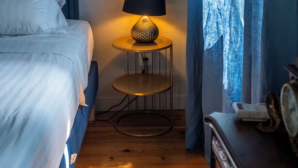 A bedroom with a bed, a round table with a lamp, a dresser, and a window with curtains. - Maison Bacchus 31 (Buzet-sur-Tarn)