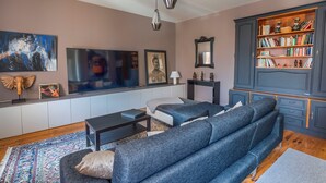 A living room with a sofa, a coffee table, a bookshelf, and artwork on the walls. - Maison Bacchus 31 (Buzet-sur-Tarn)