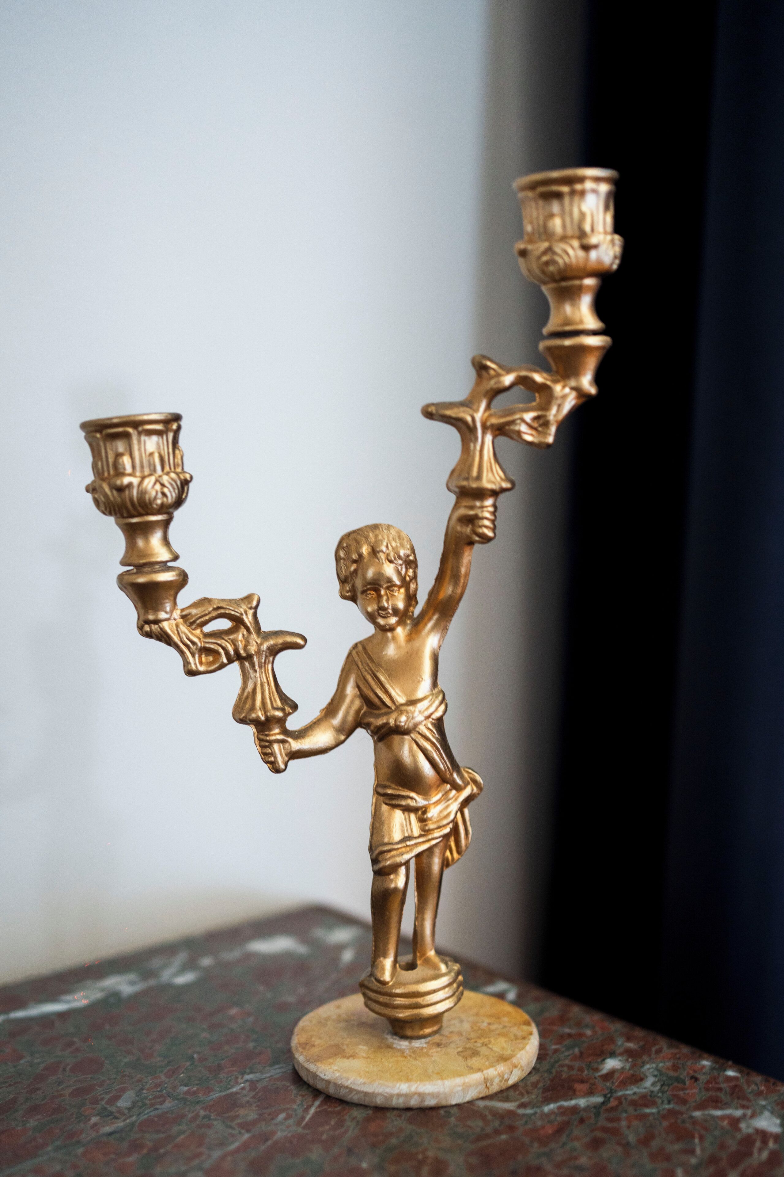 A golden candelabra with a single candle holder, a decorative figure, and a base on a marble surface.