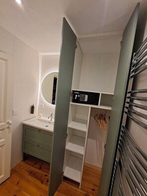 A bathroom with a sink, mirror, and open shelving unit.