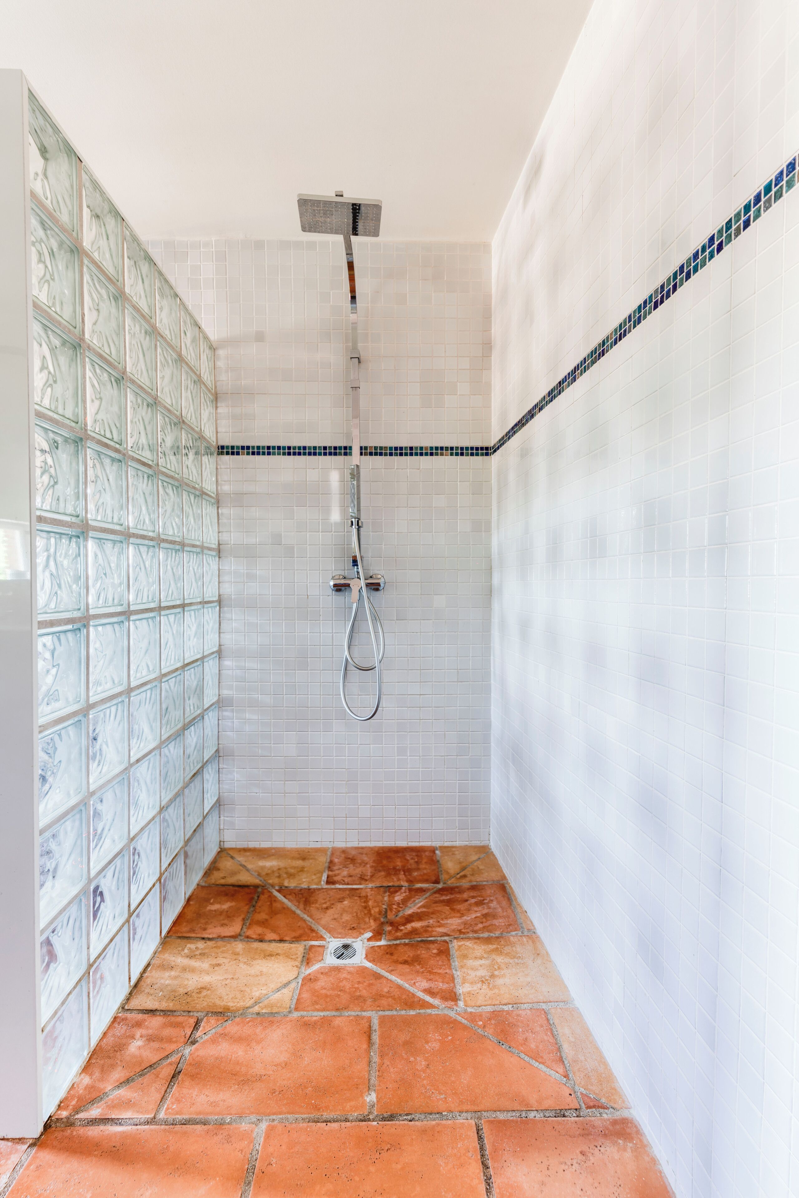 A shower with a glass door, white tiled walls, and a tiled floor.