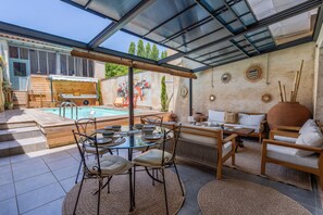 Een zonnig terras buiten, met een zwembad, eethoek en zitplaatsen.