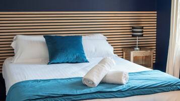 Una cama con cabecera azul, ropa de cama blanca y almohada azul.