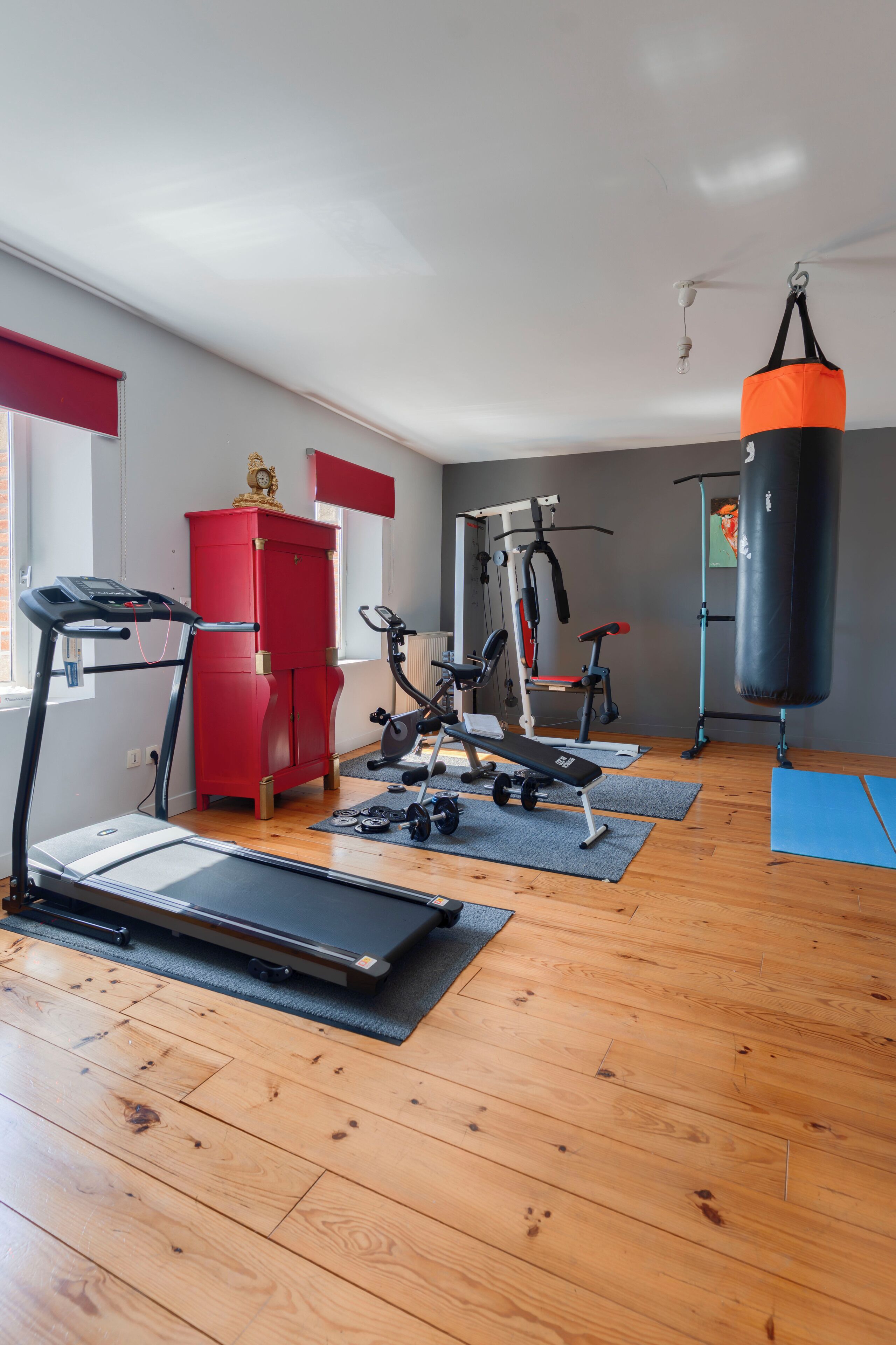 Ein Heimfitnessraum mit Laufband, Hantelbank, Kurzhanteln und einem Schlagring.