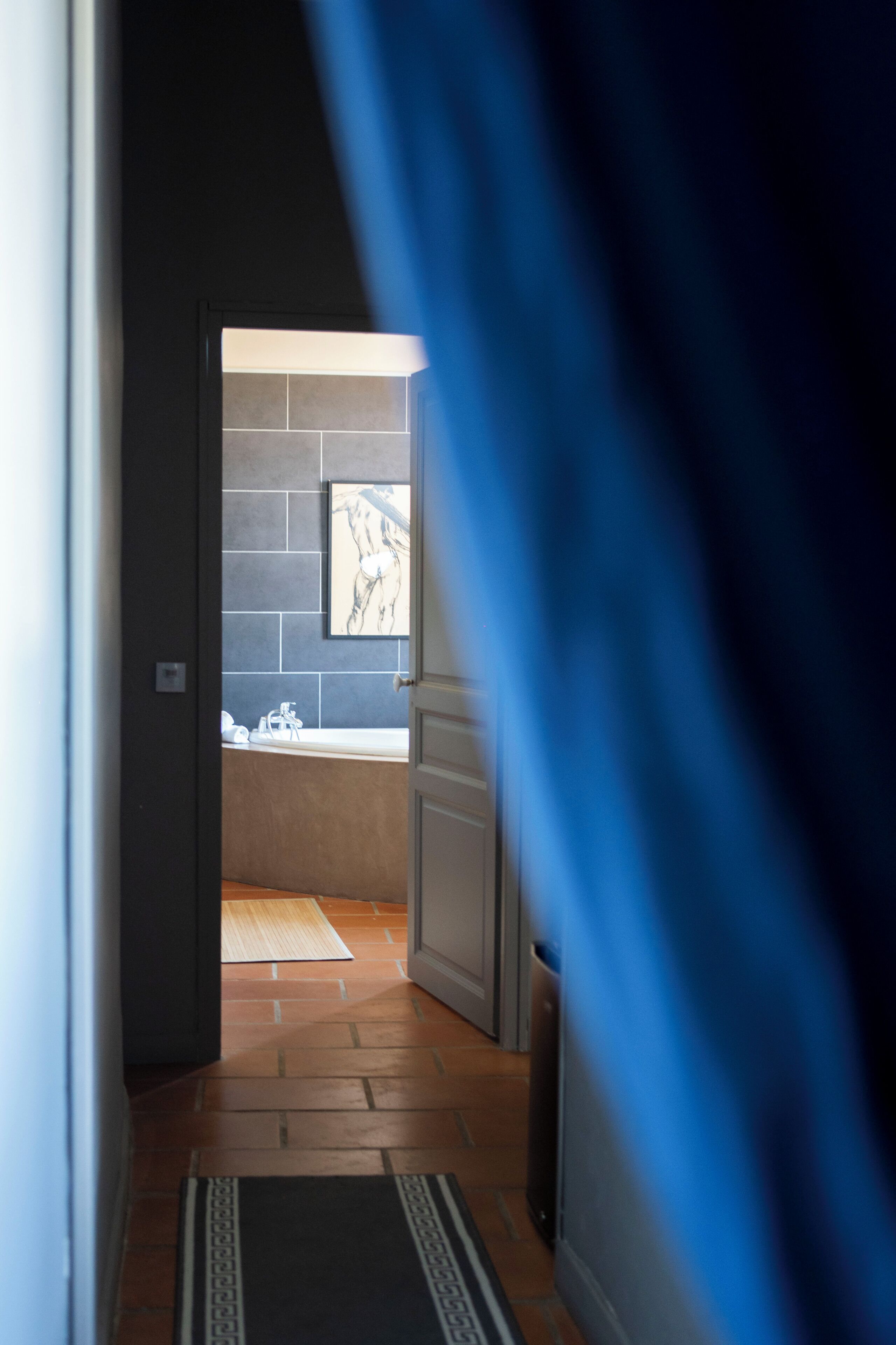 A hallway leading to a bathroom with a tiled wall, a framed artwork, and a visible toilet.