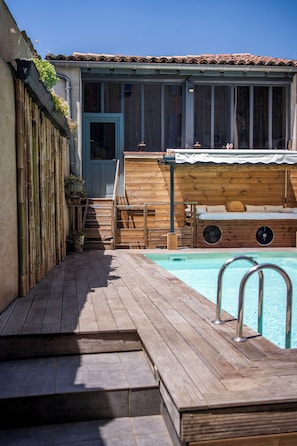 Una terraza de madera que da a una zona de piscina, con un banco de madera y un ventilador.