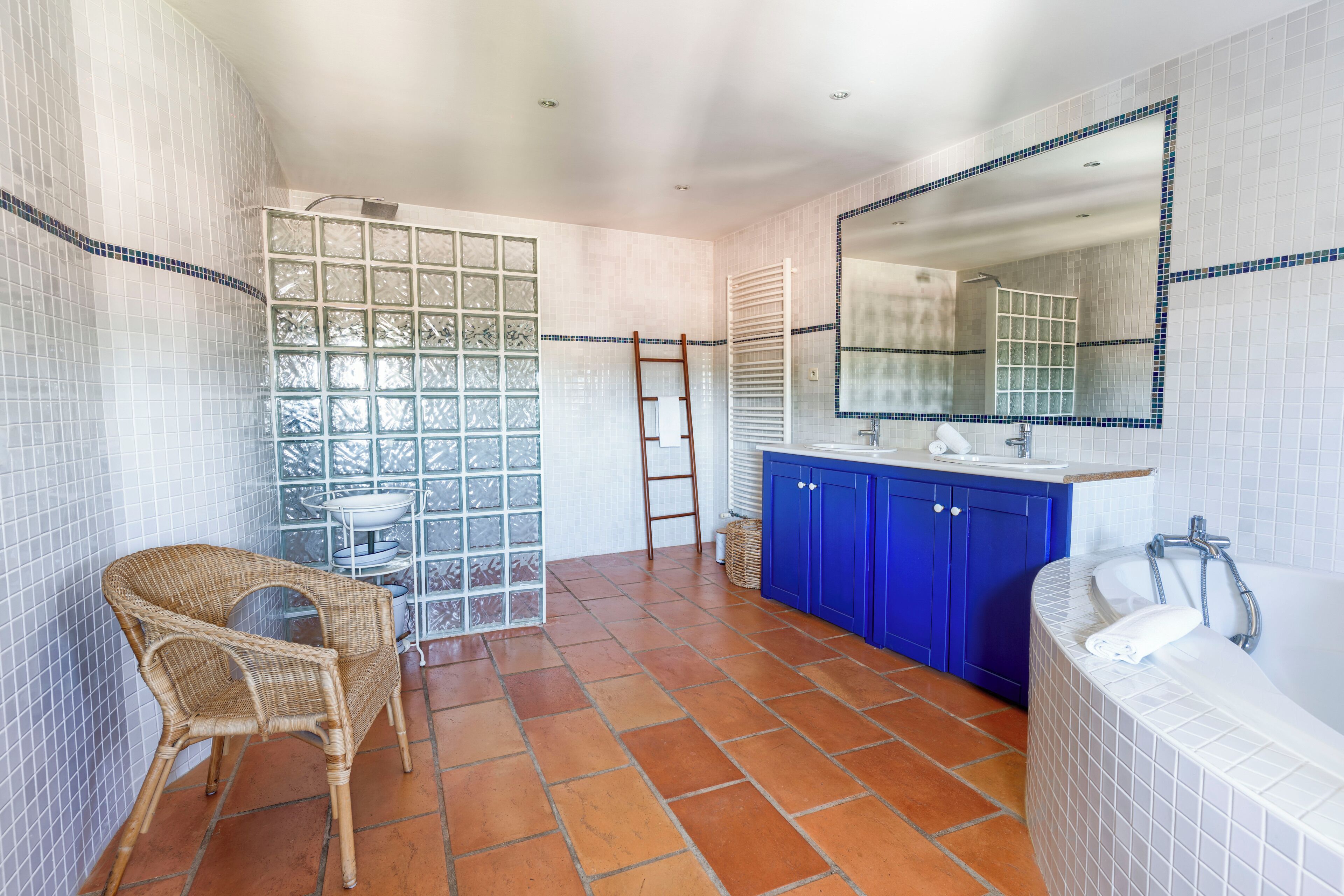 Un baño con un espejo grande, una bañera y una silla de mimbre.