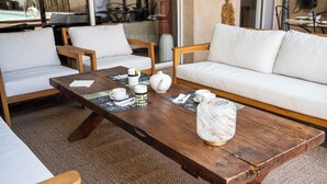 Una mesa de centro de madera con un hervidor, tazas y un jarrón decorativo en una sala de estar moderna con sofás y sillones blancos.