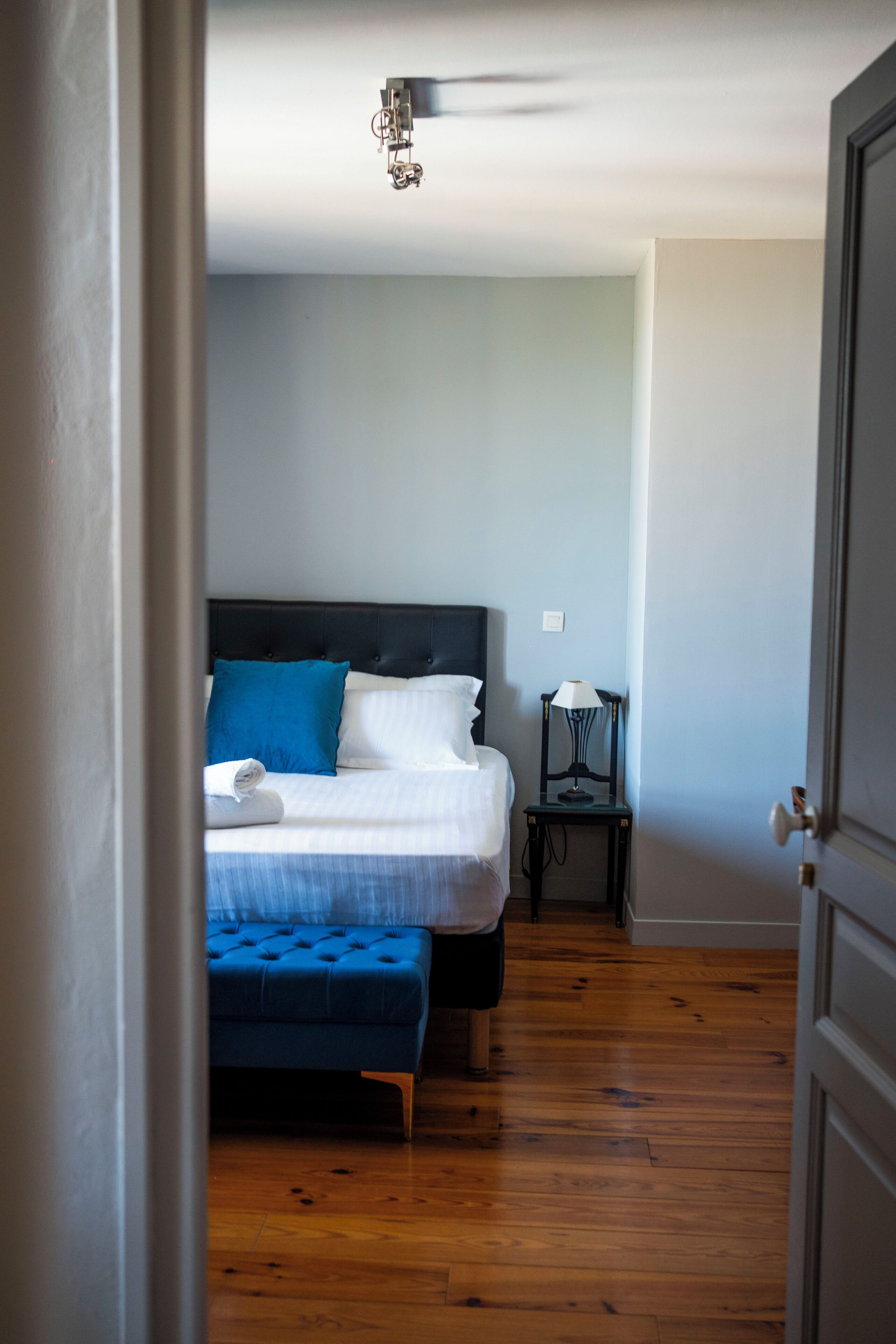 Quarto com cama, mesa de cabeceira, abajur e piso de madeira.