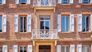 A multi-story building with a central entrance, large windows with shutters, and a decorative balcony. - Maison Bacchus 31 (Buzet-sur-Tarn)